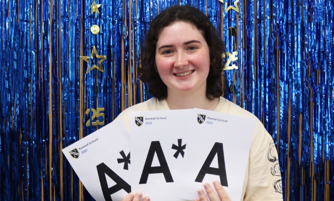 Kennet Student Clara celebrates her A Level results holding up cards of her grades against a blue foil curtain